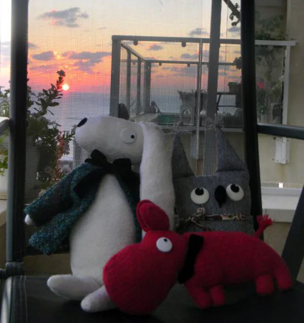Un lapin blanc, un hibou et un hippopotame rouge devant une baie vitrée, au coucher du soleil.