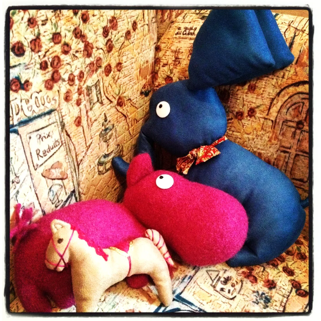 Un lapin bleu, un hippopotame rose et un petit cheval sur un canapé imprimé.