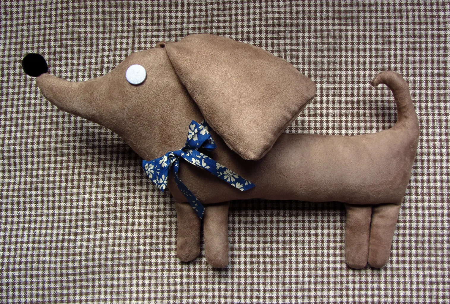 Le Basset, en toile beige aux longues oreilles, foulard bleu à fleurs, sur un tissu pied-de-poule.