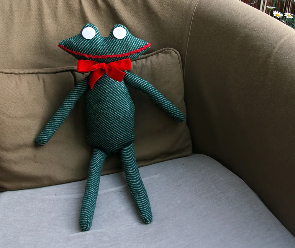 La Grenouille en tweed vert, nœud rouge, assise sur un fauteuil.